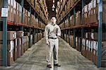 A Hispanic male warehouse worker standing next to racks of boxed products in a distribution warehouse.