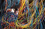 Asian male technician working on a tangled mess of CAT 5 cables in a server room.