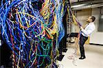 A black male technician pulling on a tangled mess of CAT 5 cables in a computer server room.