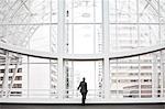 A businessman in silhouette standing at a large window in a convention centre lobby.