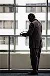 An Hispanic businessman using a notebook computer while standing in front of a window in a convention centre lobby.