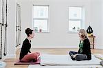 Two women sitting crossed legged facing each other in an exercise studio