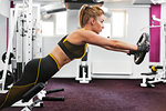 Woman lifting weight disc and leaning forward in gym