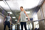 Trainer watching female client lift barbell in gym