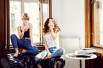 Two young female friends sitting on living room armchair drinking water