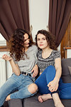 Two young female friends sitting on sofa portrait