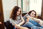Two young female friends sitting on armchair