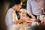 Mother serving carrots to daughter in paper crown at Christmas dinner