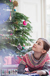 Curious girl with gift looking up at Christmas tree