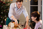 Son serving Christmas turkey to senior mother at candlelight dinner table