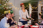 Smiling woman in paper crown serving Christmas pudding with fireworks to family at dinner table
