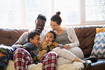 Multi-ethnic young family relaxing in pajamas on living room sofa