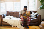 Affectionate father in pajamas cuddling with baby son on living room sofa