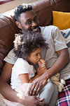 Portrait affectionate father cuddling with toddler daughter sucking thumb on sofa