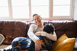Happy, carefree mother cuddling with son on living room sofa