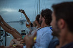 Four friends sitting on boat at dusk, drinking wine, taking selfie, British Virgin Islands