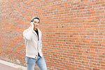 Young man talking on phone while walking along brick wall, Vancouver, Canada