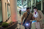 Business people with smart phone and bicycle reviewing paperwork on urban street at night