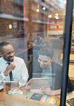 Smiling business people using digital tablet, working at cafe window