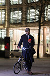 Businessman with bicycle using smart phone on urban sidewalk at night