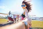 Personal perspective woman leading man by the hand toward prop airplane