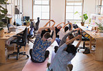 Creative business people stretching, practicing yoga in office