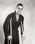 1940s SMILING MAN LOOKING AT CAMERA WEARING ROBE WALKING ON CRUTCHES