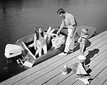 1970s FAMILY OF THREE FATHER MOTHER SON LOADING PICNIC COOLERS TOYS AND WATER SKIS INTO OUTBOARD MOTOR BOAT DOCKSIDE