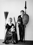 1960s PORTRAIT ODD TEEN FAMILY ALL LOOKING AT CAMERA FATHER HOLDING SPEAR SHIELD FENCING MASK MOTHER OLD BROOM AND BABY DAUGHTER