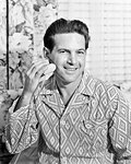 1950s SMILING MAN IN BATHROOM WEARING PAJAMAS LOOKING AT CAMERA SHAVING USING ELECTRIC RAZOR