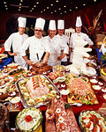 1980s FIVE SMILING CHEFS STANDING BEHIND IMMENSE BUFFET OF MEAT AND MAIN COURSE FOOD PREPARATIONS