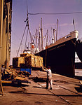 1950s WHARF SIDE INDIVIDUAL PALLETS OF FREIGHT BEING LOADING ON TO OR UNLOADING OFF FROM A TRAMP STEAMER OCEAN GOING FREIGHTER