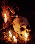 1970s HUMAN SKULL WITH BLOODY TRENCH KNIFE PROTRUDING FROM TOP SURROUNDED BY BURNING CANDLES