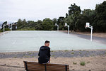 Male teenage basketball player looking back from park bench by basketball court