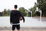Male teenage basketball player looking out over basketball court, rear view