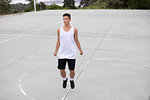 Male teenage basketball player on basketball court skipping