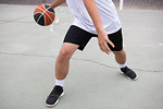 Male teenage basketball player playing basketball on court, waist down