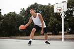 Male teenage basketball player playing basketball on court