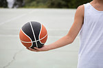 Male teenage basketball player holding ball on basketball court, cropped