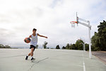 Male teenage basketball player running with ball on basketball court