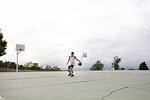 Male teenage basketball player practicing with ball on basketball court