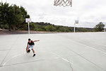 Male teenage basketball player practicing with ball near basketball hoop