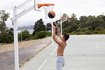 Male teenage basketball player throwing ball toward basketball hoop