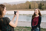 Girlfriends taking photograph by river, Belluno, Veneto, Italy