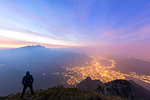 Hiker on Monte Coltignone looks toward Monte Resegone and Lecco at dawn, Lombardy, Italian Alps, Italy, Europe