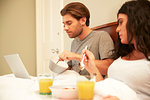 Couple using laptop while having fruit and orange juice breakfast in bed