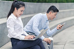 Young businesswoman and man using laptop and looking at smartphone on city seat, Shanghai, China