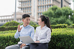 Young businesswoman and man using laptop and chatting on city seat, Shanghai, China