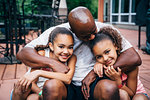Portrait of happy dad hugging daughters in front of house