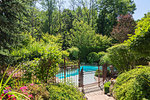 Outdoor swimming pool surrounded by wrought iron security fence and various shrubs and trees in luxury residential backyard